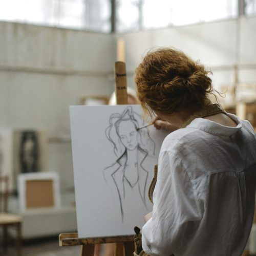 Jeune femme de dos en train de peindre dans son atelier. Elle fait partie des artistes qui exposeront pour l'ENSBA